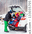 Father with his children enjoying holiday time together, sitting in snowy car trunk filled with colorful Christmas gifts. 133035705