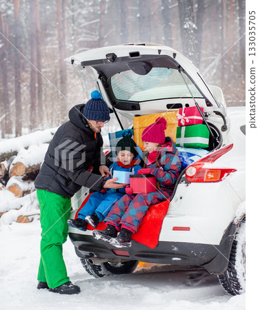 Father with his children enjoying holiday time together, sitting in snowy car trunk filled with colorful Christmas gifts. Father with his children enjoying holiday time together, sitting in snowy car trunk filled with colorful Christmas gifts. 133035705