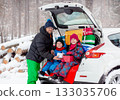 Father with his children enjoying holiday time together, sitting in snowy car trunk filled with colorful Christmas gifts. 133035706