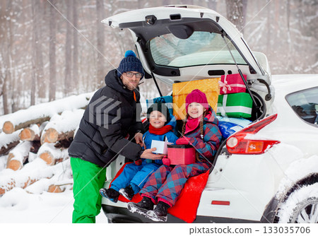 Father with his children enjoying holiday time together, sitting in snowy car trunk filled with colorful Christmas gifts. Father with his children enjoying holiday time together, sitting in snowy car trunk filled with colorful Christmas gifts. 133035706