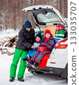 Father with his children enjoying holiday time together, sitting in snowy car trunk filled with colorful Christmas gifts. 133035707