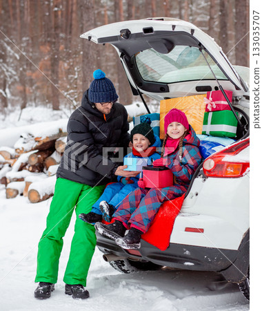 Father with his children enjoying holiday time together, sitting in snowy car trunk filled with colorful Christmas gifts. 133035707