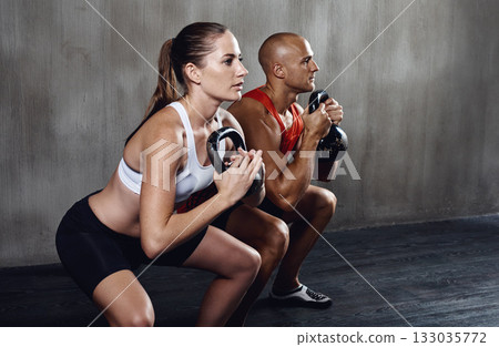 Fitness, people and workout with kettlebell in squat for weightlifting or exercise together at gym. Serious man and woman lifting weight for strong exercising, power or glutes in training indoors Fitness, people and workout with kettlebell in squat for weightlifting or exercise together at gym. Serious man and woman lifting weight for strong exercising, power or glutes in training indoors 133035772