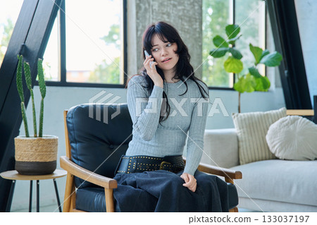 Young woman sitting at home in chair talking on cellphone 133037197