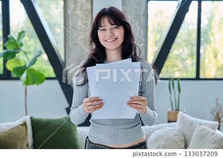 Smiling young woman with business study important papers standing in home interior 133037209