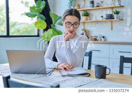 Teenage girl student sitting at the table with laptop, textbooks in home interior 133037274