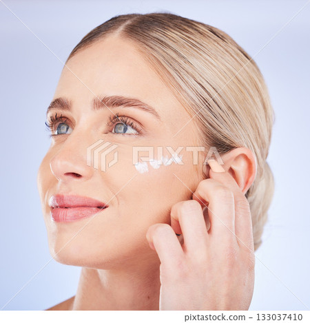 Beauty, face skincare and woman with cream in studio isolated on a blue background. Dermatology cosmetics, thinking and happy female model apply lotion, creme or moisturizer product for healthy skin. 133037410
