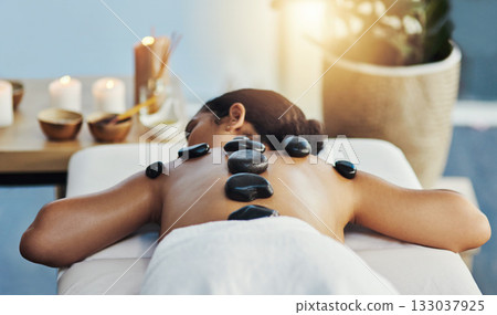 Woman, relax and rock in back massage at spa for skincare, beauty or body treatment on bed at resort. Calm female lying in relaxation with hot rocks or stone pile in therapy, zen or wellness at salon 133037925