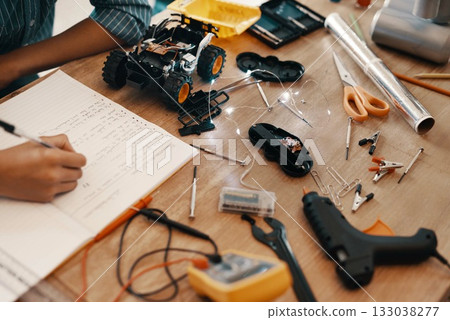 Engineering, person hand with notebook for homework and stationary or robot toys on desk at home. Technology, education or creative and male child writing or research information with pen in book 133038277