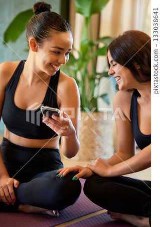 Woman, friends and yoga with phone laughing for social media, funny joke or meme while relaxing on mat. Happy and healthy yogi women laugh for fun online post on smartphone in spiritual wellness 133038641