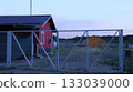 Red farmhouse behind white metal gates and orange building in the distance, farm provincial landscape with residential and outbuildings, no people, farmer's housing in the countryside 133039000