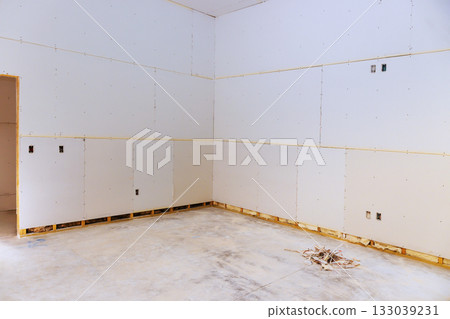 Construction site with unfinished drywall installation in bare room during renovation process 133039231
