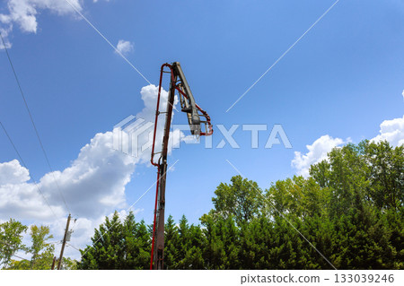 Construction crew using lift to work on tall structure under blue sky with clouds 133039246