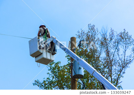 Worker uses bucket truck to repair power lines on sunny afternoon in suburban area 133039247
