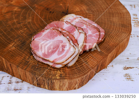 Slices of cured meat displayed on rustic wooden cutting board in home kitchen setting 133039250