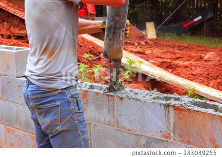 Construction worker pouring concrete into masonry block wall during home project Construction worker pouring concrete into masonry block wall during home project 133039255