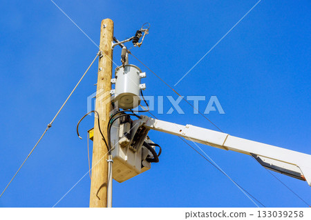 Workers performing maintenance on an electrical transformer atop utility pole under clear blue skies Workers performing maintenance on an electrical transformer atop utility pole under clear blue skies 133039258