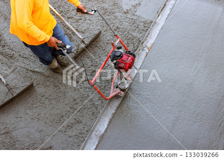 Construction worker uses power trowel to smooth concrete during building project Construction worker uses power trowel to smooth concrete during building project 133039266