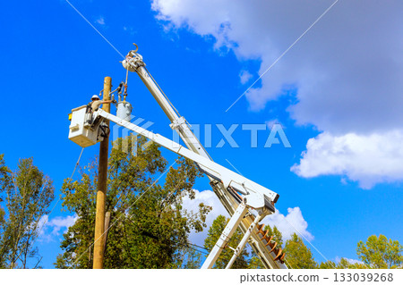 Utility worker repairs electrical equipment on pole under clear blue sky in suburban area 133039268
