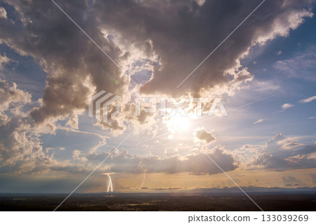 Dramatic thunderstorm with lightning over green landscape during sunset in rural area Dramatic thunderstorm with lightning over green landscape during sunset in rural area 133039269
