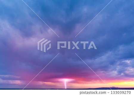 Colorful sunset sky with dramatic lightning striking over horizon during stormy evening Colorful sunset sky with dramatic lightning striking over horizon during stormy evening 133039270