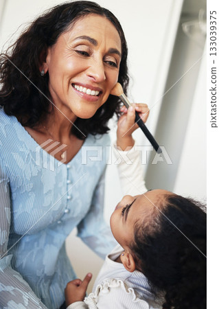 Happy child doing makeup of a grandmother for fun, bonding and family quality time. Comic, smile and girl applying facial cosmetics for a senior woman, playing and blending blush on the face Happy child doing makeup of a grandmother for fun, bonding and family quality time. Comic, smile and girl applying facial cosmetics for a senior woman, playing and blending blush on the face 133039375