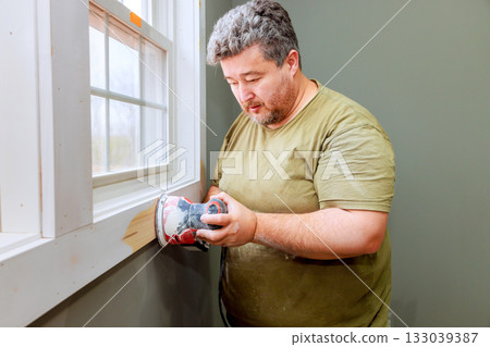 Man sanding wood near window during home renovation project Man sanding wood near window during home renovation project 133039387