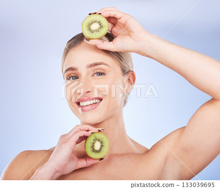 Portrait, kiwi and woman with skincare, cosmetics and smile with girl against a blue studio background. Face, female and lady with fruit, morning routine or grooming for smooth, clear or natural care Portrait, kiwi and woman with skincare, cosmetics and smile with girl against a blue studio background. Face, female and lady with fruit, morning routine or grooming for smooth, clear or natural care 133039695