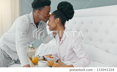 Breakfast in bed, love and black couple kissing on their honeymoon, birthday or anniversary in a hotel room. Happy man and woman bonding in a bedroom for love while on vacation or holiday together Breakfast in bed, love and black couple kissing on their honeymoon, birthday or anniversary in a hotel room. Happy man and woman bonding in a bedroom for love while on vacation or holiday together 133041104