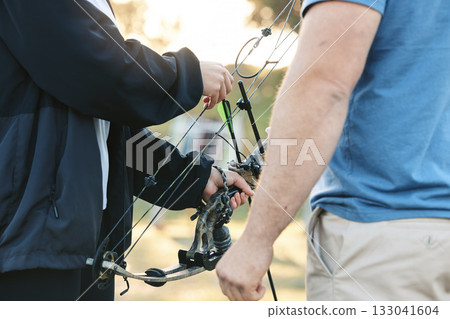 Shooting range, bow and archery sports training with a woman and man outdoor for target practice. Hands of archer and athlete person for competition game or learning to aim, exercise and shoot arrow Shooting range, bow and archery sports training with a woman and man outdoor for target practice. Hands of archer and athlete person for competition game or learning to aim, exercise and shoot arrow 133041604