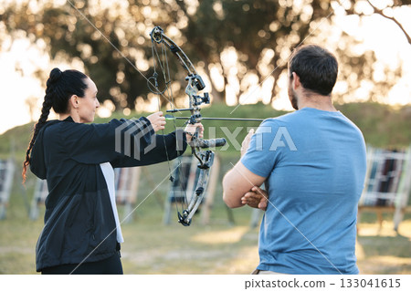 Woman, archery and target training with an instructor on a field for hobby, aim and control. Arrow, practice and archer people together outdoor for hunting, precision and weapon, shooting competition 133041615