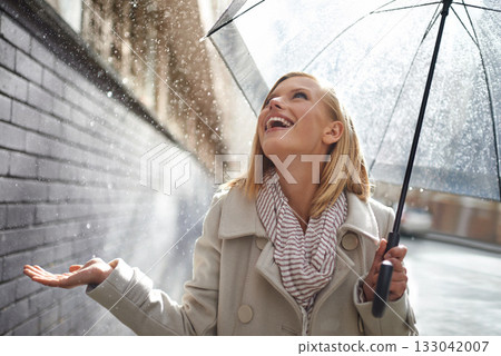 Smile, excited woman and rain in the city with umbrella, freedom and happiness on holiday. Winter weather, raining or urban street with a young female person on a sidewalk and travel vacation outdoor 133042007