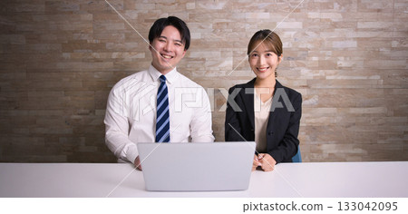 辦公室裡,一對面帶著笑容的年輕男女並排坐著。 辦公室裡,一對面帶著笑容的年輕男女並排坐著。 133042095