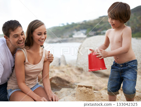 Child, family and sand castle at beach in summer for fun, travel or holiday with a smile. A man, woman and excited kid playing together on vacation at sea with a toy bucket, development and happiness Child, family and sand castle at beach in summer for fun, travel or holiday with a smile. A man, woman and excited kid playing together on vacation at sea with a toy bucket, development and happiness 133042325