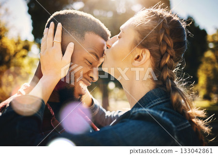 Interracial couple, forehead kiss and smile in nature for love, bonding and embracing relationship. Happy woman kissing man on head smiling for loving care, affection or embrace in a park outdoors 133042861