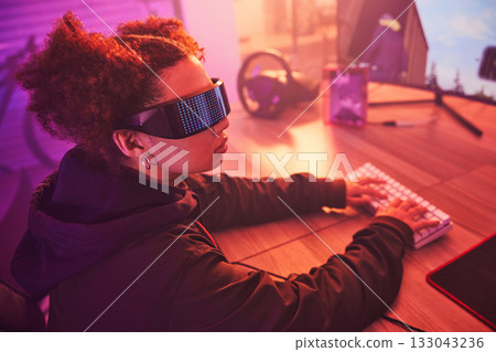 Hacker, cyber security and programming with black woman typing for coding, software and phishing. Neon, night and network with girl programmer at desk for ransomware, technology and developer 133043236
