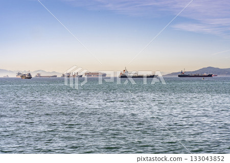 Cargo Ships Anchored in the Gibraltar bay with a misty African coast behind 133043852