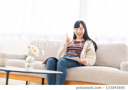 Young woman sitting on sofa and reading a magazine Young woman sitting on sofa and reading a magazine 133043895
