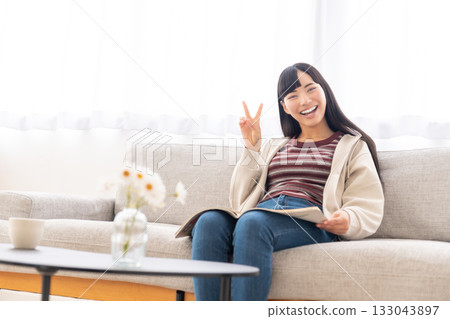 Young woman sitting on sofa and reading a magazine Young woman sitting on sofa and reading a magazine 133043897
