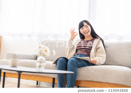 Young woman sitting on sofa and reading a magazine Young woman sitting on sofa and reading a magazine 133043898