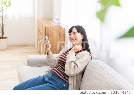 年輕女子坐在沙發上,用智慧型手機聽音樂。 年輕女子坐在沙發上,用智慧型手機聽音樂。 133044143