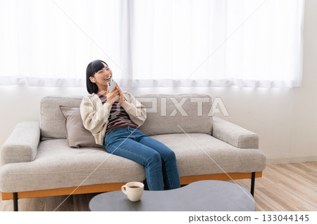 Young woman sitting on sofa and listening to music on smartphone Young woman sitting on sofa and listening to music on smartphone 133044145