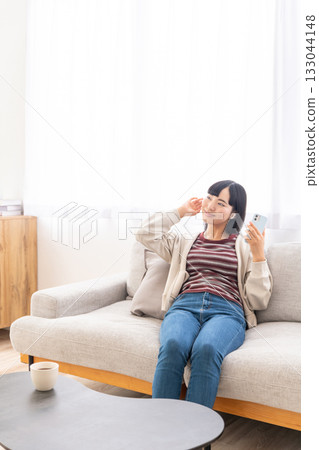 年輕女子坐在沙發上,用智慧型手機聽音樂。 年輕女子坐在沙發上,用智慧型手機聽音樂。 133044148