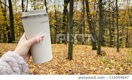Hand holding a thermal mug on an autumn walk. Horizontal shot of a park path with fallen leaves Hand holding a thermal mug on an autumn walk. Horizontal shot of a park path with fallen leaves 133044647