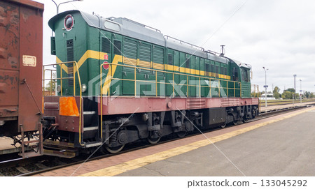 Powerful diesel locomotive pulls a heavy freight car. Freight train on the tracks, seen from behind. Summer clouds loom Powerful diesel locomotive pulls a heavy freight car. Freight train on the tracks, seen from behind. Summer clouds loom 133045292