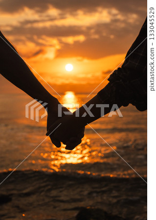 Silhouette of couple holding hands at sunrise on the beach with golden sunlight reflecting on the calm sea Silhouette of couple holding hands at sunrise on the beach with golden sunlight reflecting on the calm sea 133045529