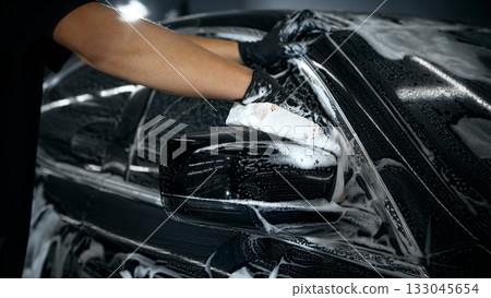 Hands washing car mirror with foam sponge during auto detailing 133045654