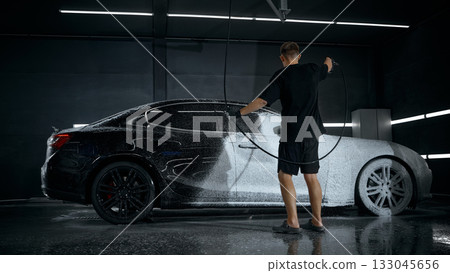 Worker washing luxury car with foam sprayer inside modern detailing bay 133045656