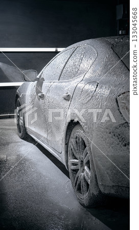 Black car completely covered in snow foam under bright wash lights 133045668