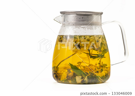 A glass pitcher filled with a yellowish tea and herbs A glass pitcher filled with a yellowish tea and herbs 133046009